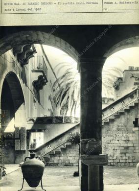 Archivio fotografico Galleria Reg. di Palazzo Bellomo, Stampa fotografica in bianco e nero di formato non indicato, risalente a circa il 1942, dopo i lavori di restauro del palazzo, atti ad istituire il Museo Nazionale. La stampa è posta sul cartoncino dell’Archivio fotografico della Galleria Reg. di Palazzo Bellomo, già Museo Nazionale. Il soggetto è una veduta della prima rampa della scala in stile catalano, ripresa dal portico del piano terra, da cui si possono notare le decorazioni a traforo del corrimano. L’autore è Angelo Maltese di Siracusa., Stampa in B/N da pellicola, CC BY-NC-ND