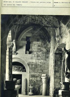 Archivio fotografico Galleria Reg. di Palazzo Bellomo, Stampa fotografica in bianco e nero di formato non indicato, risalente a prima del 1952, prima dei lavori di ristrutturazione del palazzo. La stampa è posta sul cartoncino dell’Archivio fotografico della Galleria Reg. di Palazzo Bellomo, già Museo Nazionale. Il soggetto è uno scorcio del portico al piano terra del palazzo, con l’esposizione di reperti architettonici bizantini del Museo. L’autore è Angelo Maltese di Siracusa., Stampa in B/N da pellicola, CC BY-NC-ND