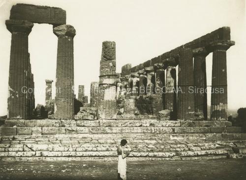 Fotografia artistica F. Galifi Crupi, Taormina (nel verso timbro a inchiostro), Agrigento, veduta del Tempio di Giunone Lacinia (V sec. a. C.). In posa aggraziata, al centro dello spazio scenografico, un giovane a torso nudo e con un panno in vita, XIX-XX secolo, stampa su carta gelatina ai sali d'argento (positivo 29390), collocazione C1_ID_039_FGC_001, CC BY-NC-ND Fotografia artistica F. Galifi Crupi, Taormina (nel verso timbro a inchiostro), Agrigento, veduta del Tempio di Giunone Lacinia (V sec. a. C.). In posa aggraziata, al centro dello spazio scenografico, un giovane a torso nudo e con un panno in vita, XIX-XX secolo, stampa su carta gelatina ai sali d'argento (positivo 29390), collocazione C1_ID_039_FGC_001, CC BY-NC-ND