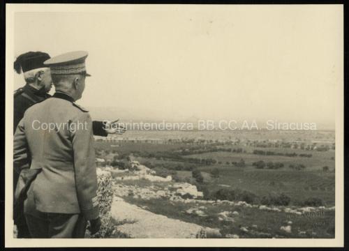 C. Consoli, Catania (nel recto in basso a destra timbro a secco), Vittorio Emanuele III in visita al Castello Eurialo di Siracusa, con lui Giuseppe Cultrera Soprintendente alle Antichità della Sicilia Orientale. Sullo sfondo la pianura, di contrada Targia, con le coltivazioni agricole tipiche della zona, 1941, stampa su carta gelatina ai sali d'argento, CC BY-NC-ND C. Consoli, Catania (nel recto in basso a destra timbro a secco), Vittorio Emanuele III in visita al Castello Eurialo di Siracusa, con lui Giuseppe Cultrera Soprintendente alle Antichità della Sicilia Orientale. Sullo sfondo la pianura, di contrada Targia, con le coltivazioni agricole tipiche della zona, 1941, stampa su carta gelatina ai sali d'argento, CC BY-NC-ND