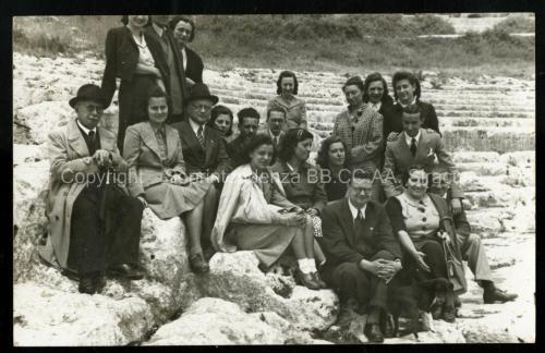 Anonimo, Giuseppe Cultrera accompagna un gruppo numeroso di visitatori al Teatro greco di Siracusa. Nel verso della cartolina fotografica viaggiata, sono apposte le firme dei partecipanti alla visita archeologica: Gabriella Mangano, Mara Maiocco, Carmelina D'Urso, Andreina Dé Morien, Liliana Rizzo, Gabriella Seva, Giuseppe Borini, Catullo Mercurelli e Tania Squarciafini, 25/05/1940, stampa gelatina ai sali d'argento su cartolina Ferrania, collocazione C2_ID_397_FGC_001, CC BY-NC-ND Anonimo, Giuseppe Cultrera accompagna un gruppo numeroso di visitatori al Teatro greco di Siracusa. Nel verso della cartolina fotografica viaggiata, sono apposte le firme dei partecipanti alla visita archeologica: Gabriella Mangano, Mara Maiocco, Carmelina D'Urso, Andreina Dé Morien, Liliana Rizzo, Gabriella Seva, Giuseppe Borini, Catullo Mercurelli e Tania Squarciafini, 25/05/1940, stampa gelatina ai sali d'argento su cartolina Ferrania, collocazione C2_ID_397_FGC_001, CC BY-NC-ND