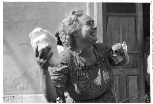 Anonimo, In Via degli Orti una fedele con in mano il cotone utilizzato per asciugare le Lacrime della Madonna. Nel suo volto un'intensa emozione per l'evento miracoloso che si stava compiendo. Da una casa due donne la osservano, 08/1953, stampa su carta gelatina ai sali d'argento, CC BY-NC-ND